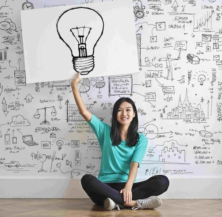 Woman sitting in front of a brainstorming wall holding a poster of a lightbulb